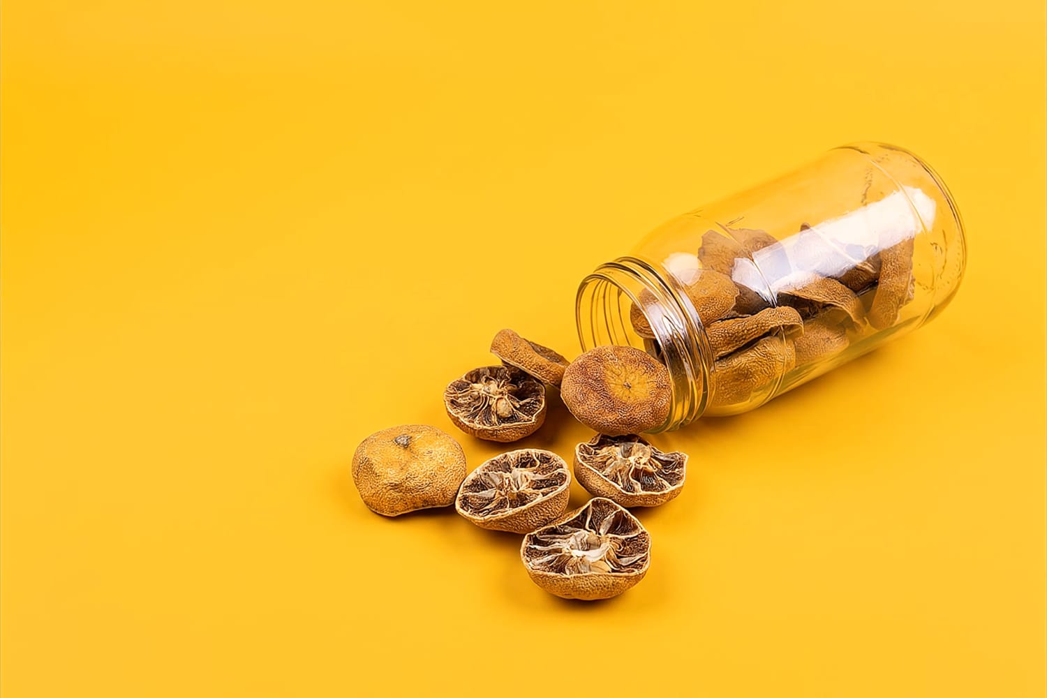 Dehydrated lemon pieces spilling from a glass jar on a yellow background
